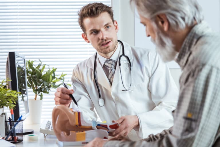 Doctor showing to senior patient a model of the human ear. Deafness treatment concept.