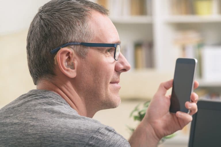 Man with a hearing aid uses smartphone.
