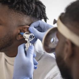 Close up of a male doctor carefully holding the ear of his patient to establish a clearer view of the inside of his ear, to see if he requires hearing aids at a modern clinic