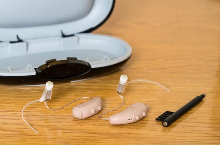 Close up of hearing aids with cleaning brush and storage case.