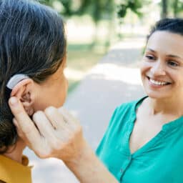 Woman with hearing aid chats with a friend outdoors.