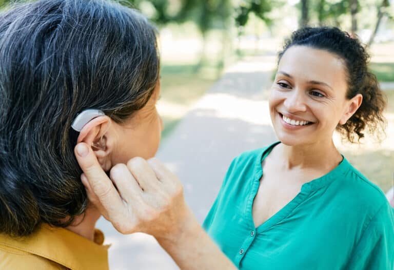 Woman with hearing aid chats with a friend outdoors.