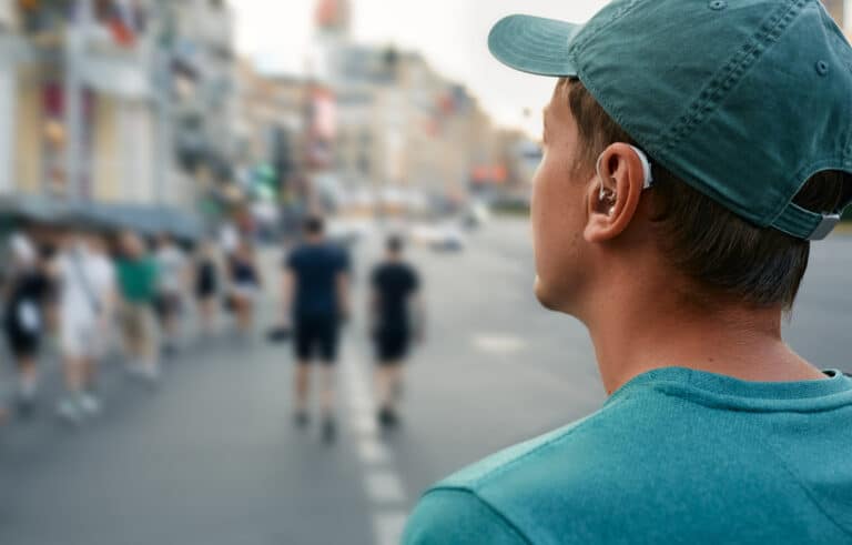 Young man with a hearing aid walking around a busy city.