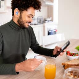 Young man with a hearing aid looks at his smartphone over breakfast.