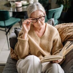 Older woman reading a book on her couch.