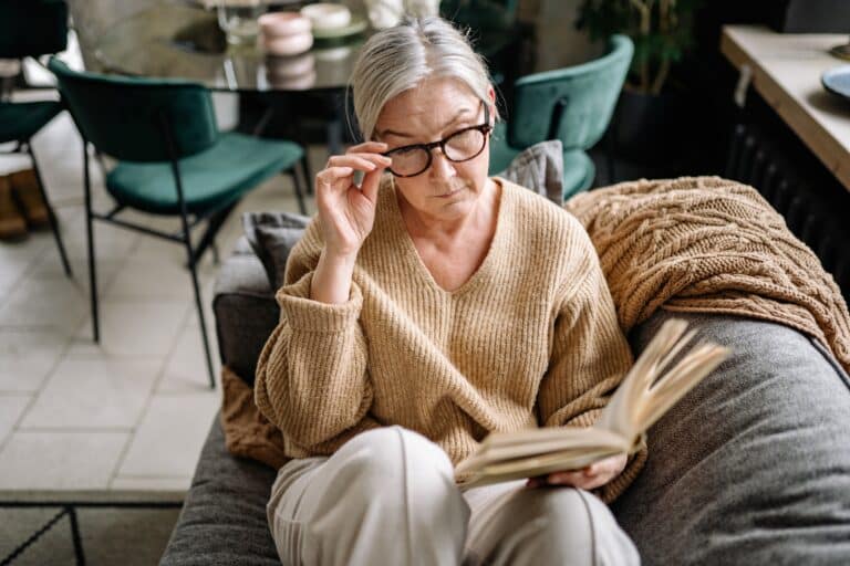 Older woman reading a book on her couch.