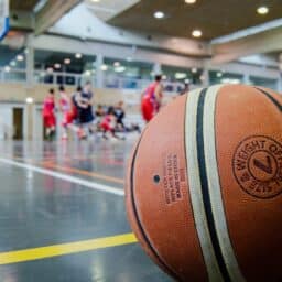 Close up of a basketball in an indoor gym with players in the background.