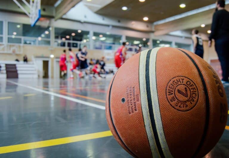 Close up of a basketball in an indoor gym with players in the background.