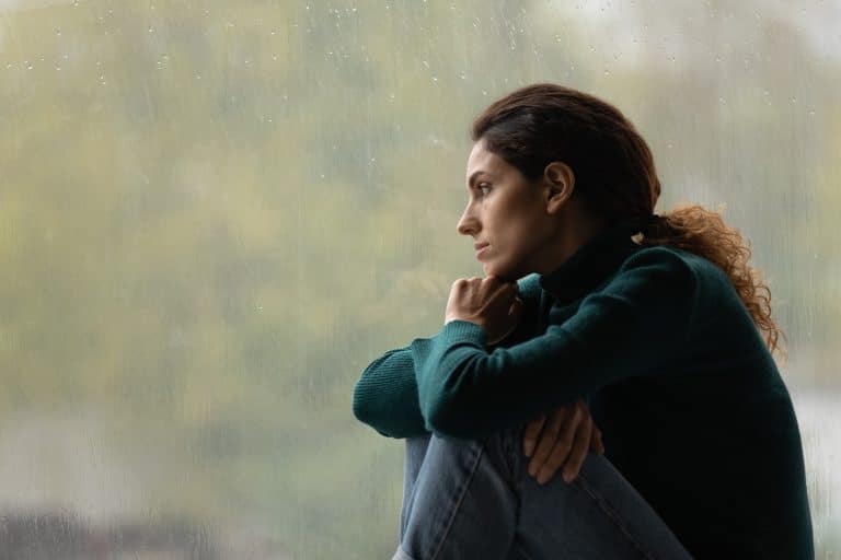 a woman looks morosely outside of a window