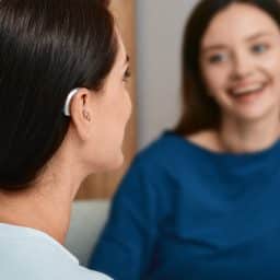 Woman with a behind-the-ear hearing aid talks with her friend at home.