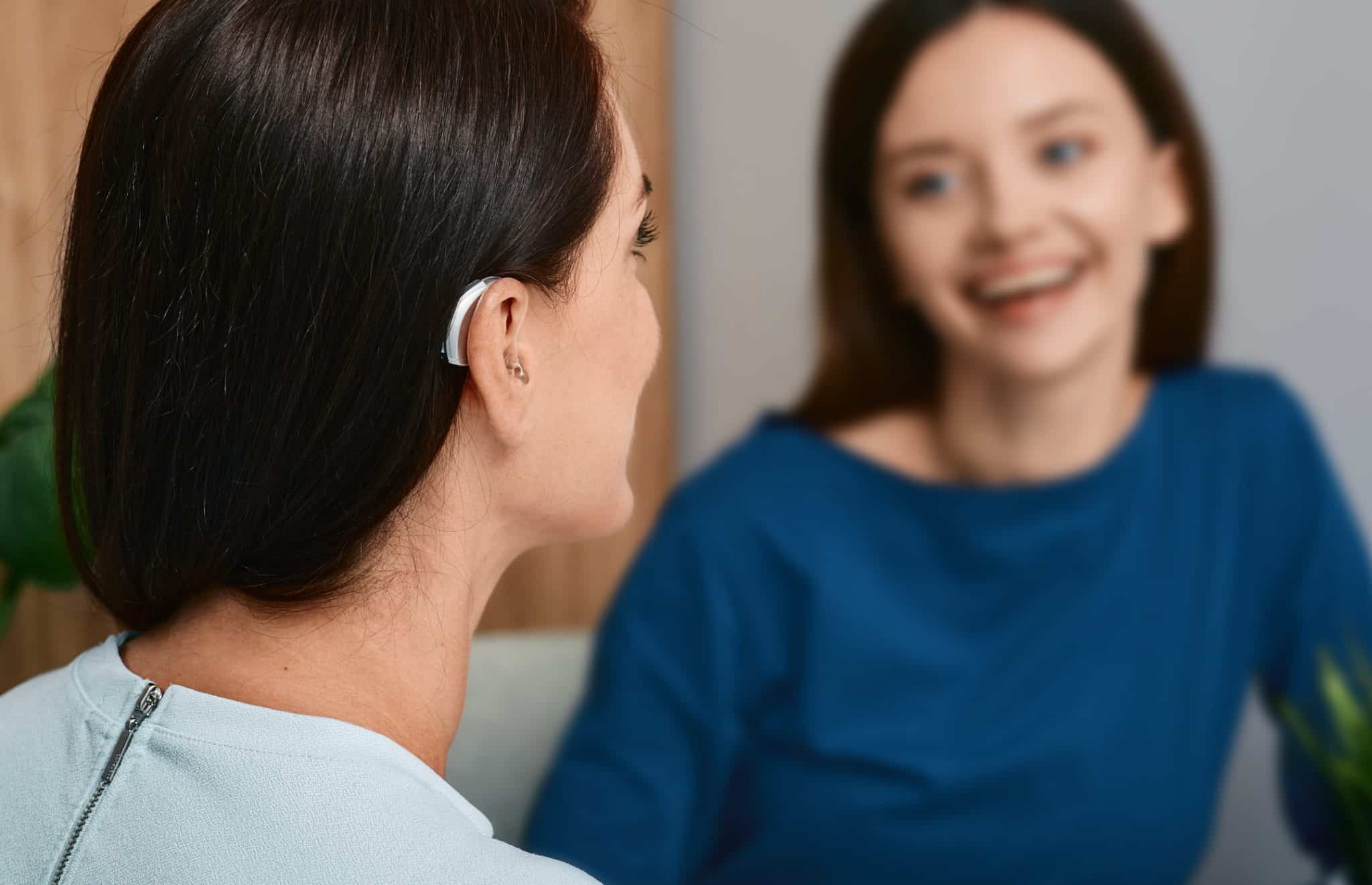 Woman with a behind-the-ear hearing aid talks with her friend at home.