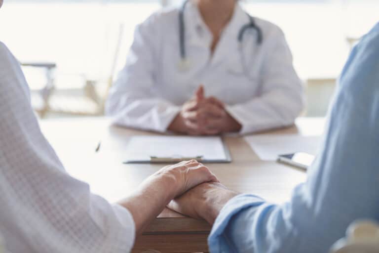 A couple holding hands at an audiology appointment