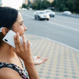 Adult woman with a hearing impairment uses a hearing aid in everyday life, talking on phone in urban city outdoor.