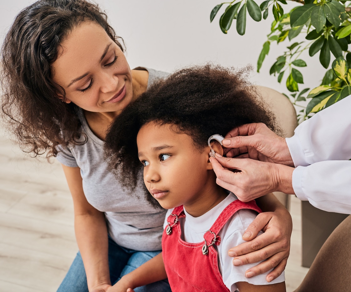 Parent helps child with hearing aid.